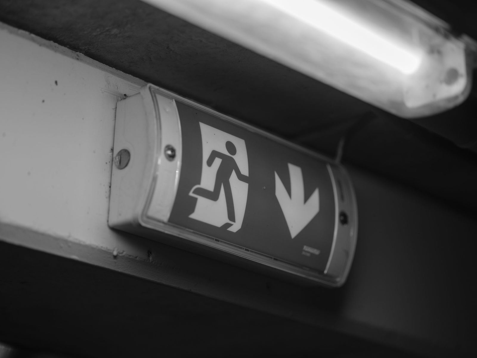 Verlicht nooduitgangbord met pictogram en pijl, onder een tl-lamp