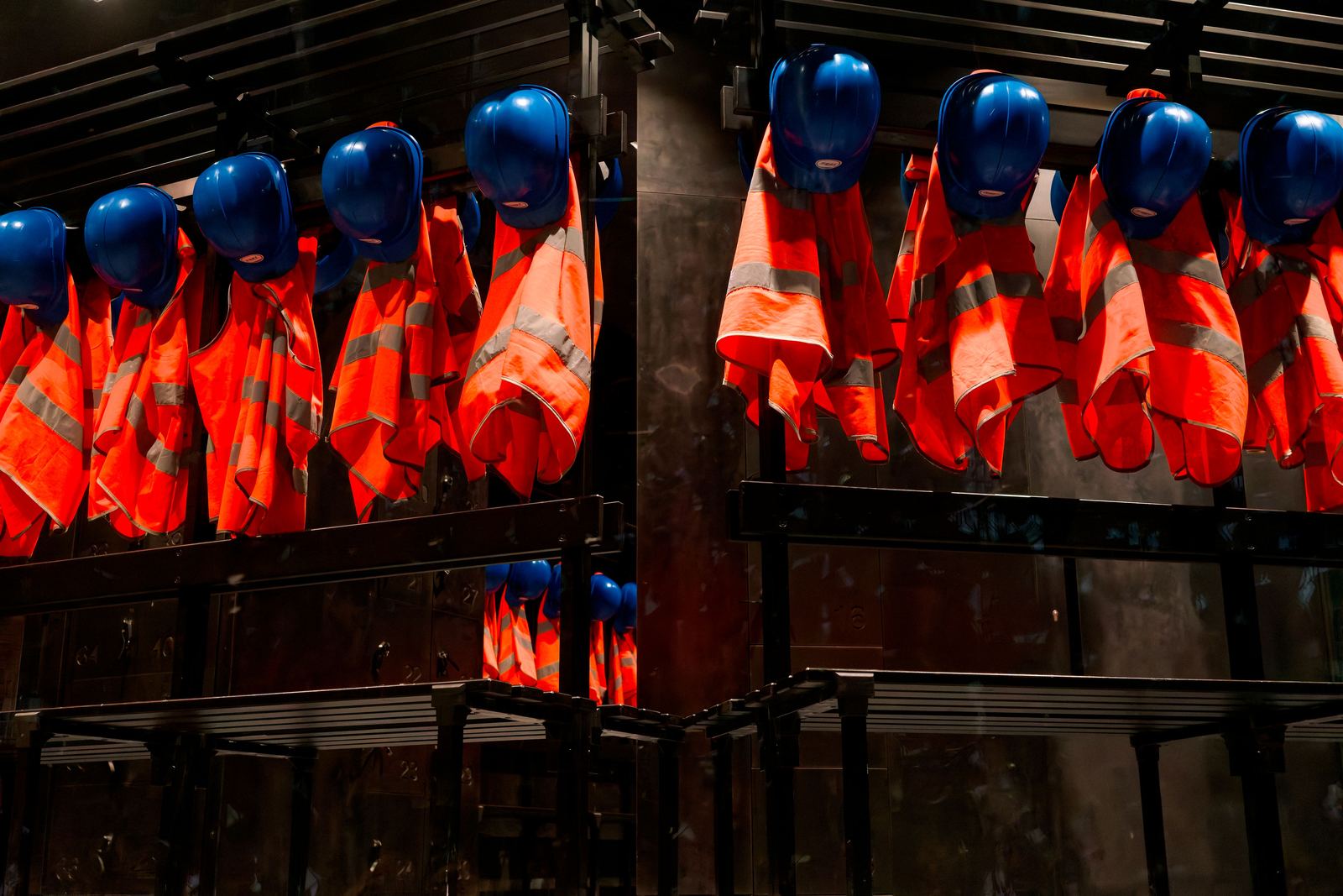 Rijen veiligheidshelmen en signalisatiehesjes die klaarhangen aan een rek