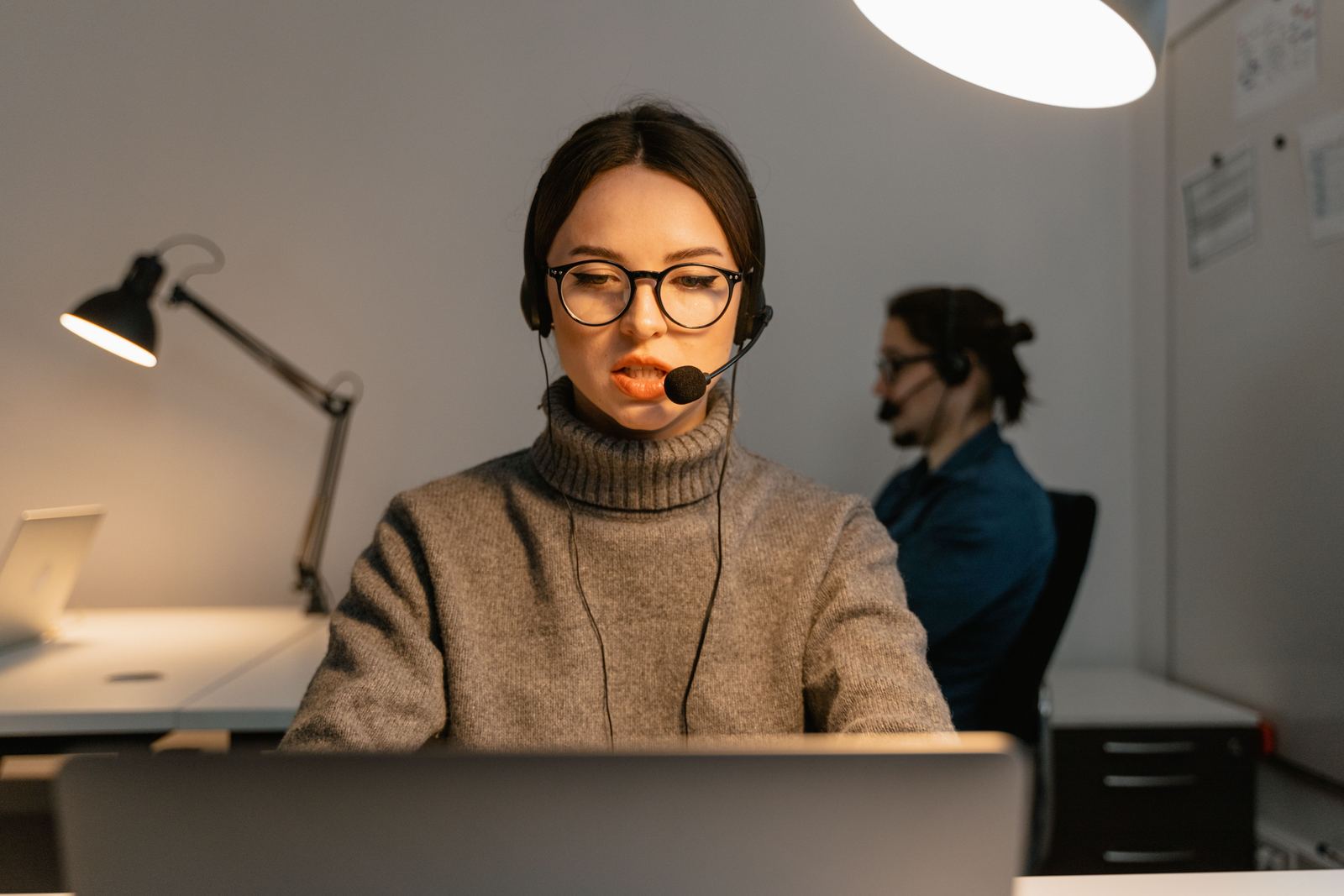 Medewerker met headset achter een scherm, laat op de dag
