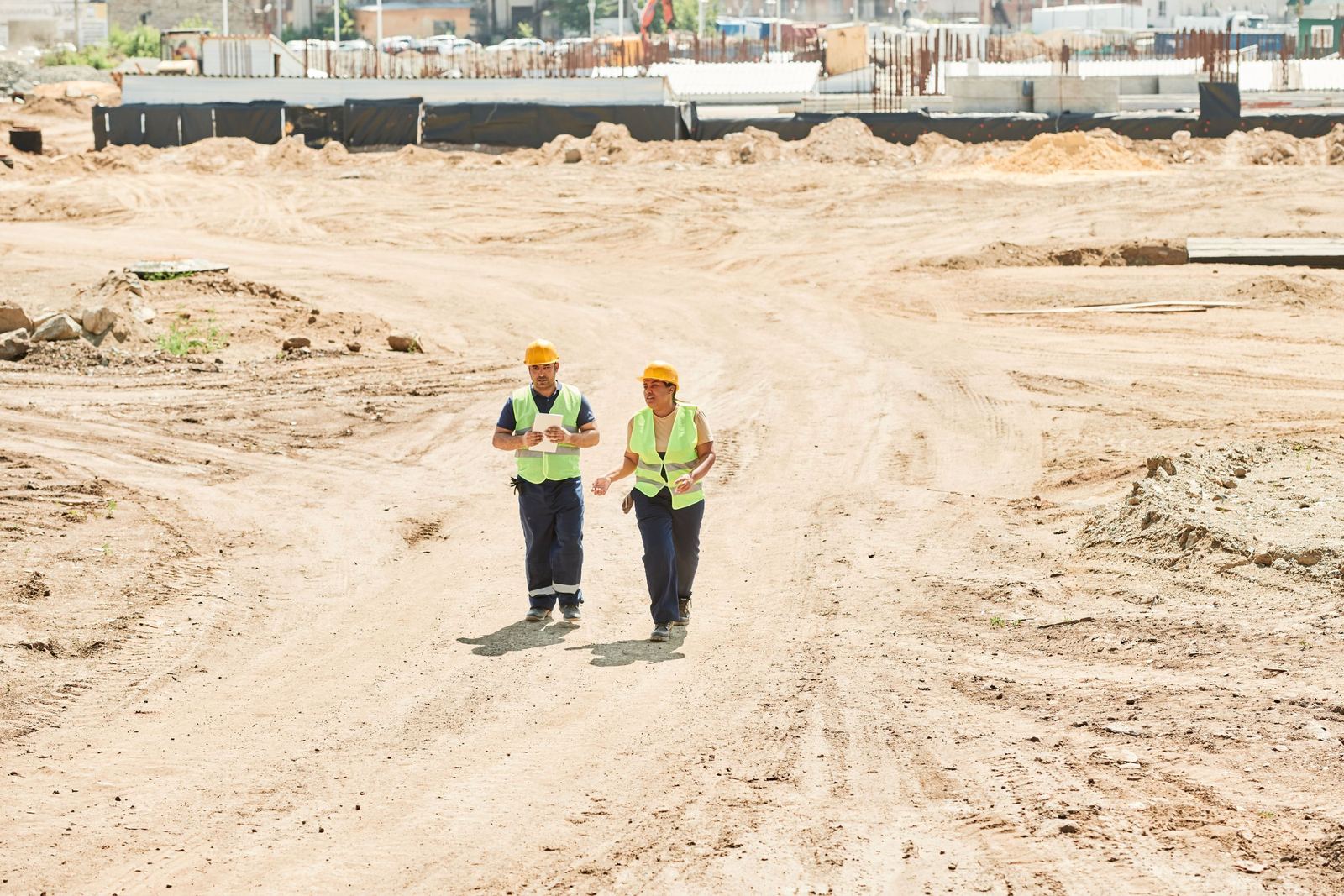 Twee mensen in signalisatiekledij en helm die pratend over een werfterrein lopen